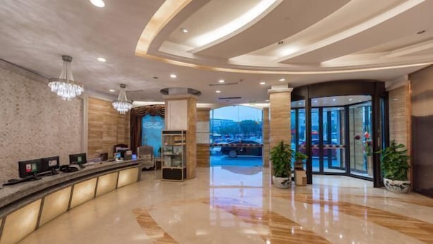 Un hall d’hôtel moderne avec un comptoir d’accueil, des lustres et une vue sur la rue.