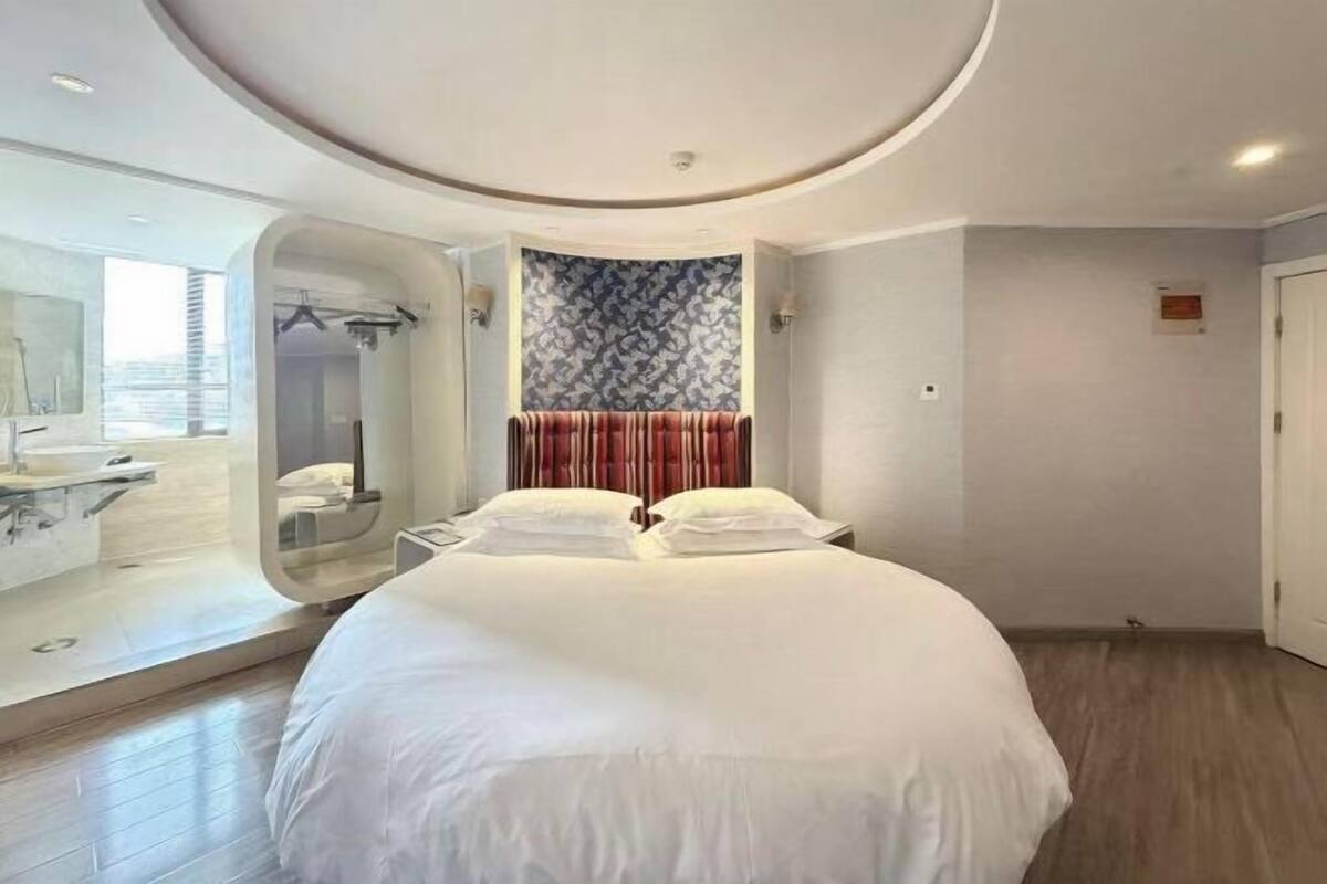 Une chambre d’hôtel moderne avec un grand lit, une salle de bain dotée d’un miroir et d’un lavabo, et un mur orné d’un motif.