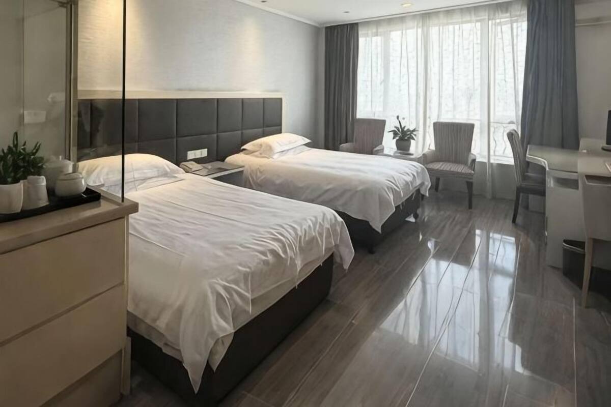 Une chambre d’hôtel avec deux lits, un bureau, une chaise et une grande fenêtre avec des rideaux.