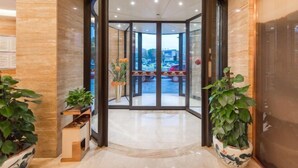 L’entrée d’un hôtel, avec une porte tournante, des plantes en pot et une vue sur le parking.