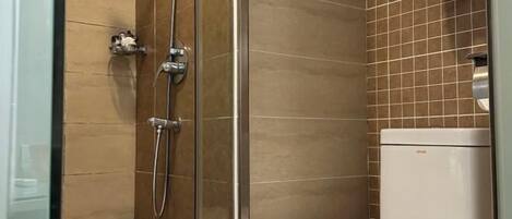 A bathroom with a glass-enclosed shower, a white toilet, and a tiled wall.