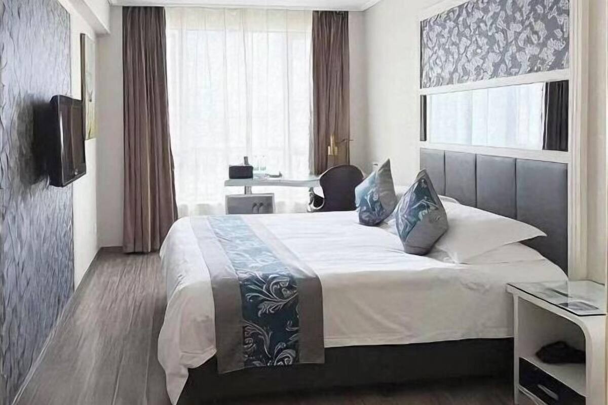Une chambre d’hôtel avec un grand lit, un bureau, une chaise et un téléviseur fixé au mur.