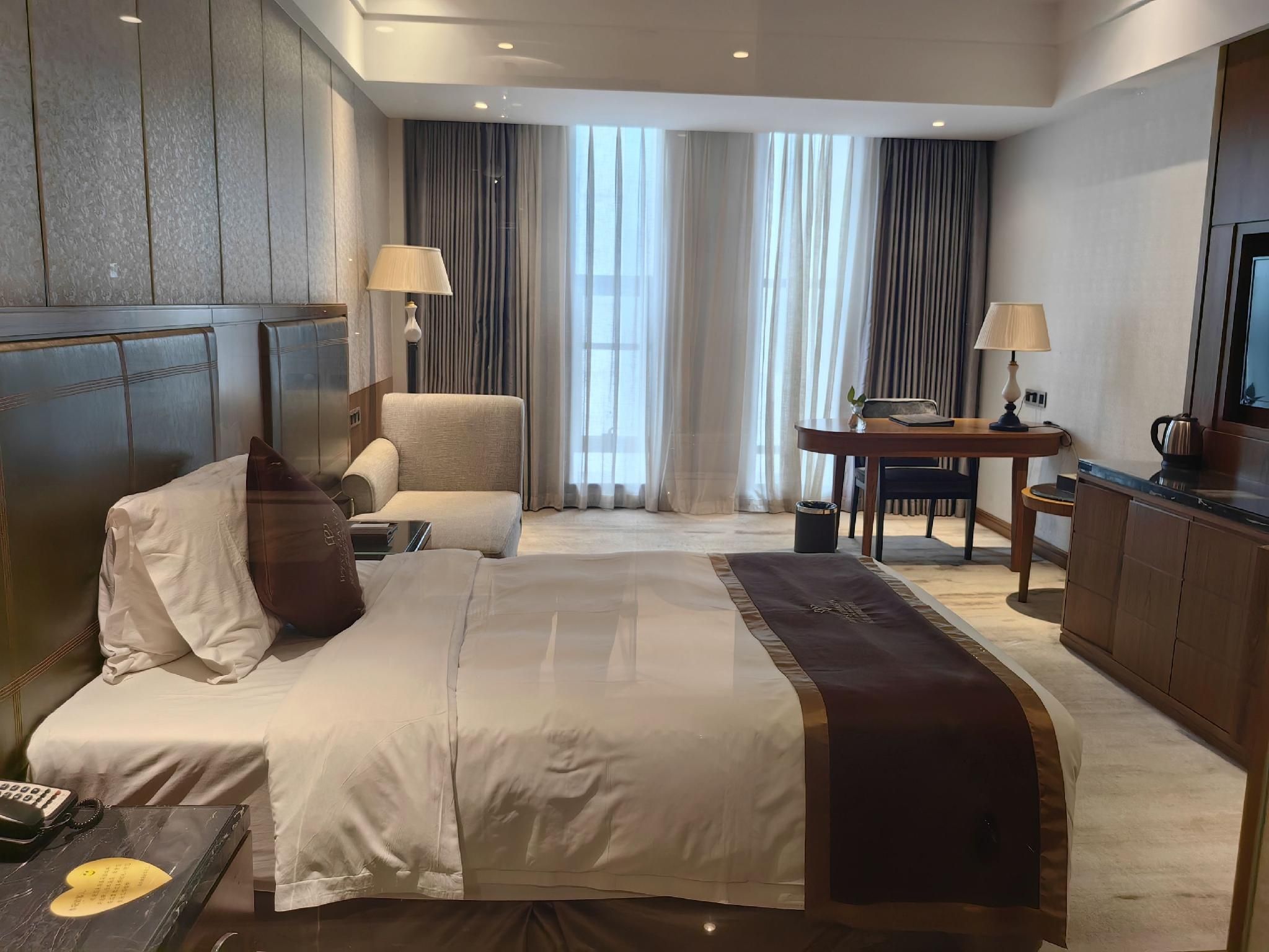 Habitación de hotel con una cama grande, un escritorio, una silla, un televisor y vistas al exterior a través de la ventana.