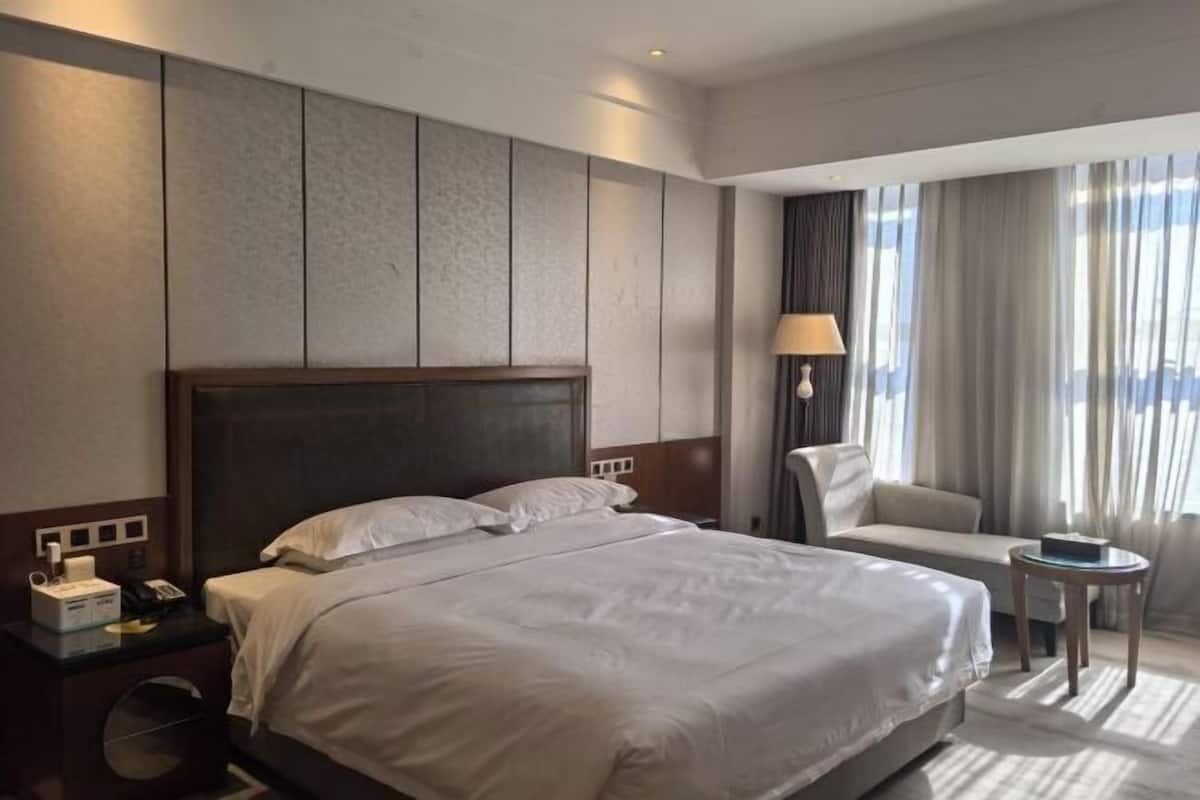 Hotellihuone, jossa on suuri sänky, yöpöytä lampun kanssa, sohva ja pieni pöytä.