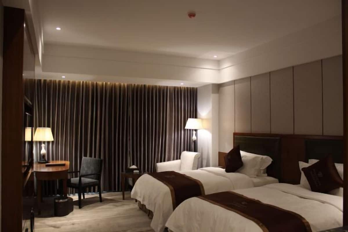 Hotellihuone, jossa on kaksi sänkyä, työpöytä, tuoli ja verhoilla varustettu tausta.
