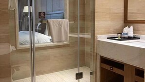 Een moderne badkamer met een glazen douchecabine, een bed met een handdoek en een wastafel met toiletartikelen.