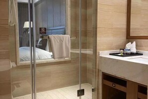 A modern bathroom with a glass shower enclosure, a visible bed with a towel, and a sink with toiletries. - Wisconsin Spa Hotel (Tianjin)