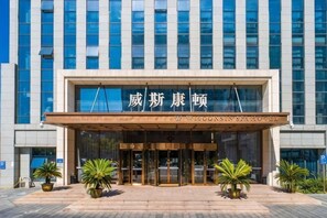 L’entrée d’un hôtel, avec une façade moderne, de grandes fenêtres en verre et une enseigne bien visible.