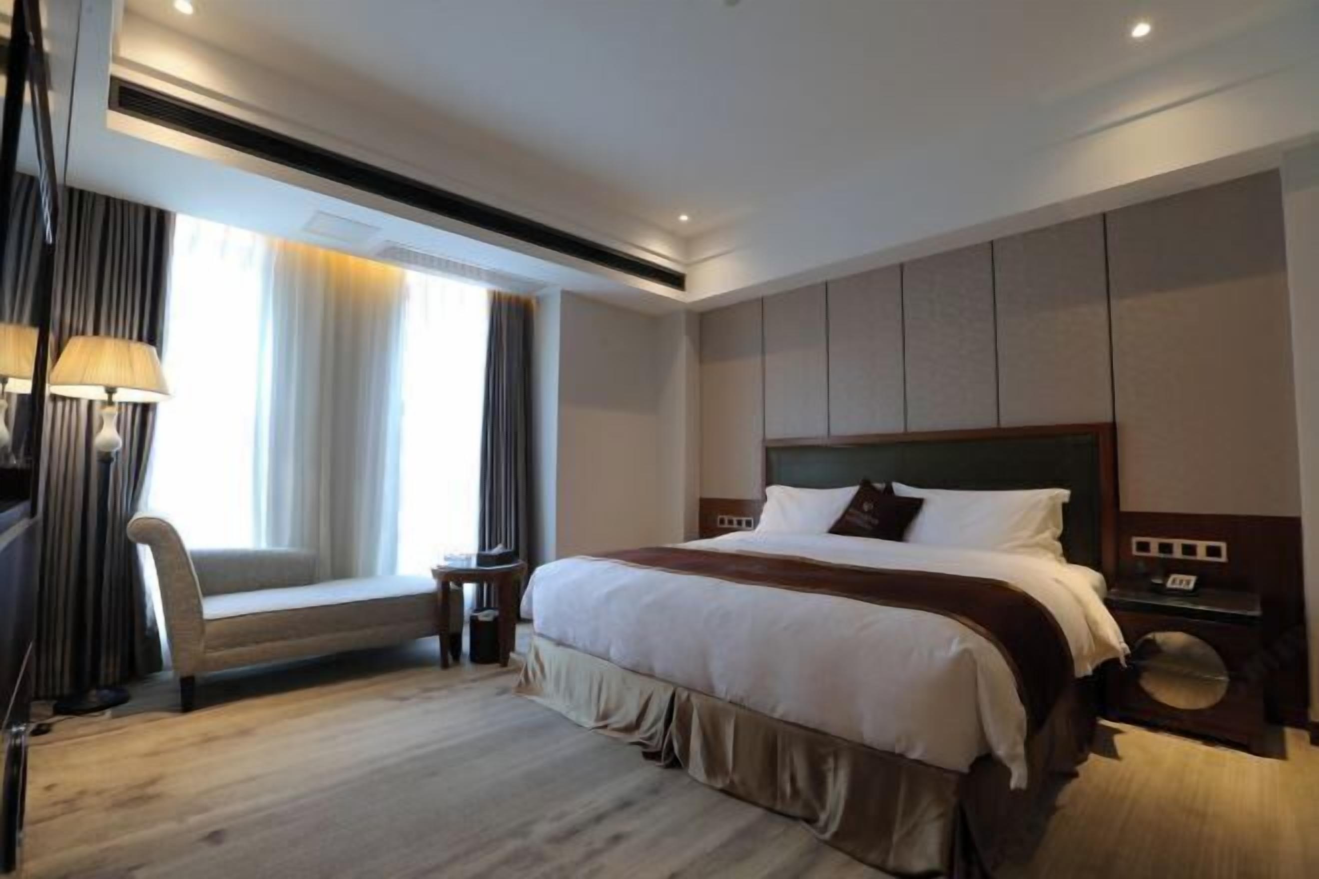 A hotel room with a large bed, a bedside table, a chair, and a window with curtains.