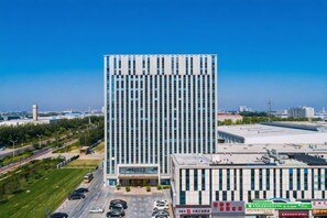 Een hoog, modern gebouw met een glazen gevel, omringd door een parkeerplaats en commerciële borden.