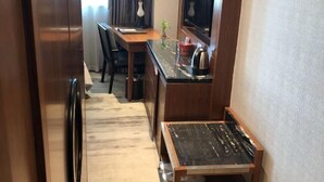 Een compacte hotelkamer met een houten bureau, een tafeltje, een spiegel en een kitchenette.