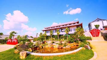 A building with a traditional architectural style, a landscaped garden with a pond, and a clear sky.