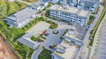 Vista aérea de um complexo moderno de edifícios, com várias estruturas, área de estacionamento e vegetação ao redor.