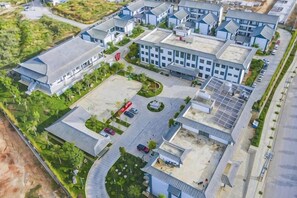 An aerial view of a modern building complex with multiple structures, a parking area, and surrounding greenery. - Taowowo Holiday Hotel (Jianshui)
