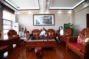 A room with a wooden coffee table, chairs, a television, and a framed picture on the wall. - Taowowo Holiday Hotel (Jianshui)