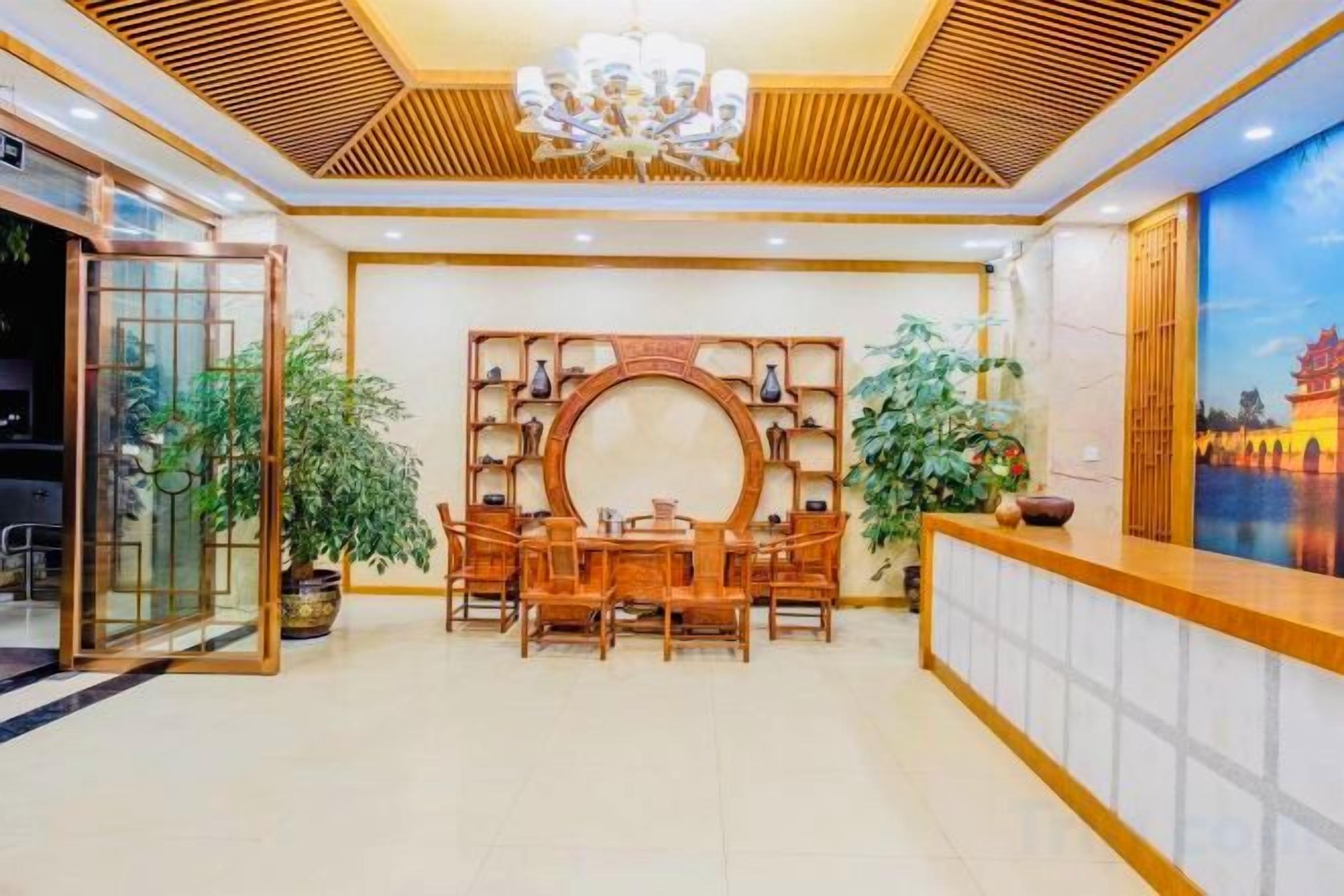 Zona de recepción con mostrador de madera, una mesa redonda con sillas y una pared decorativa con estanterías.