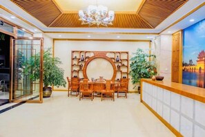 A reception area with a wooden reception desk, a round table with chairs, and a decorative wall with shelves. - Taowowo Holiday Hotel (Jianshui)