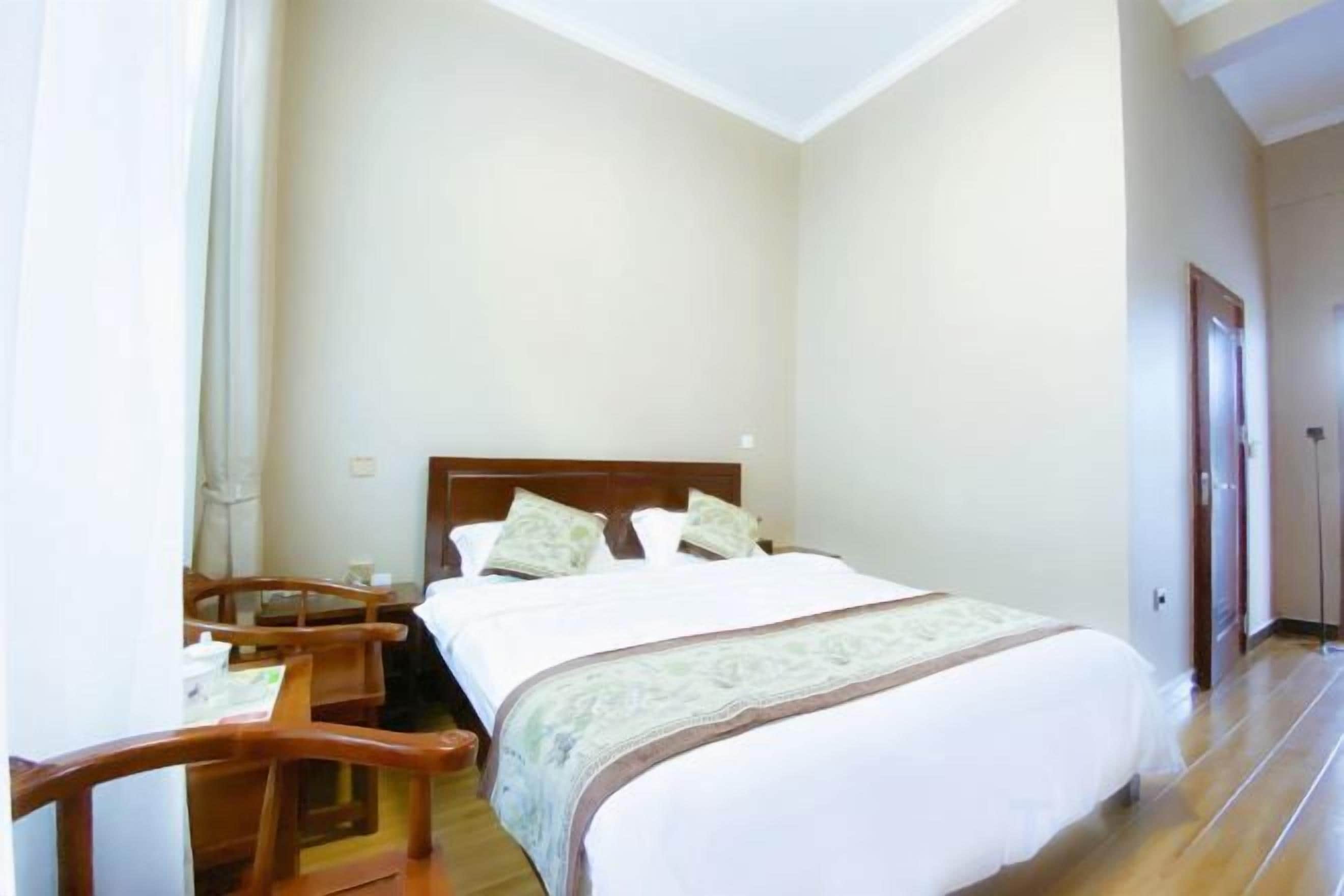 A hotel room with a bed, a wooden chair, a nightstand, and a door.