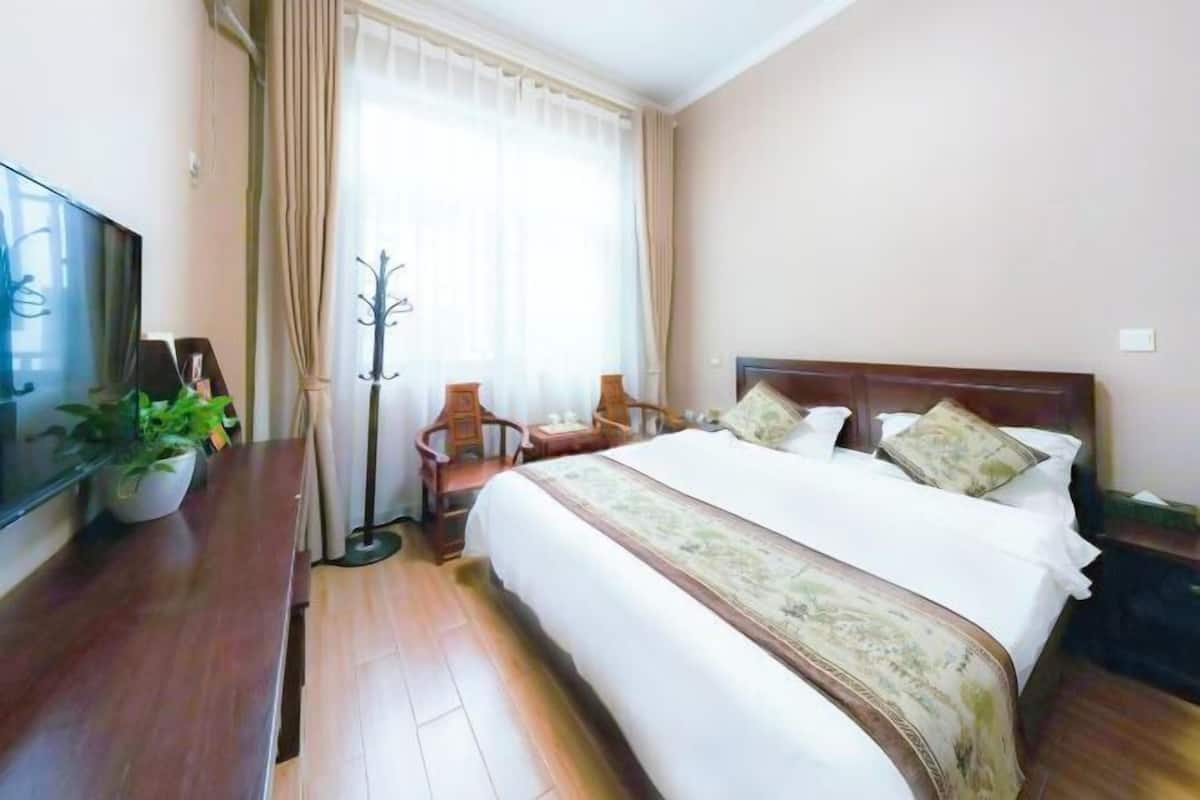 A hotel room with a bed, a TV, a desk, a chair, and a window with curtains.