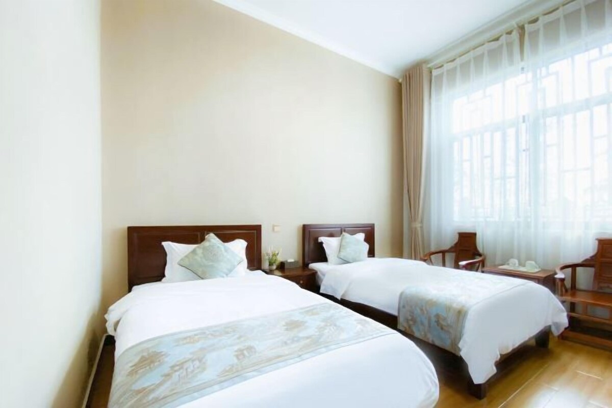 A hotel room with two beds, a wooden headboard, a nightstand, a chair, and a large window with curtains.
