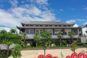 A traditional building with a tiled roof, surrounded by greenery and palm trees.