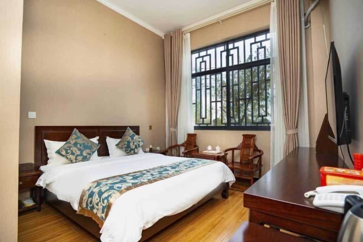 A hotel room with a bed, a desk, a chair, a TV, and a window with a metal gate.