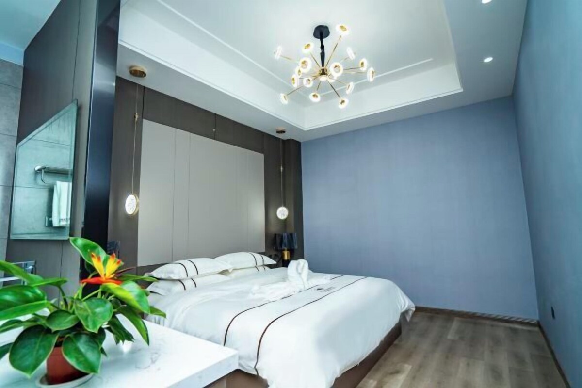 A modern bedroom with a large bed, a ceiling light fixture, and a potted plant.
