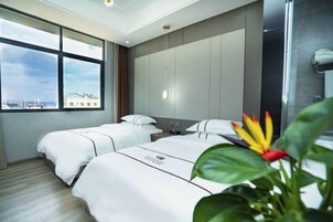 Habitación de hotel con dos camas, un ventanal grande, una planta y vistas a la ciudad.
