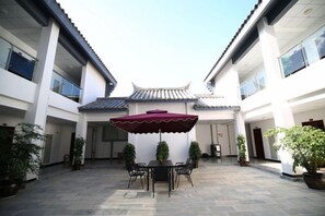 A courtyard with a table and chairs under a red umbrella, surrounded by potted plants. - Taowowo Holiday Hotel (Jianshui)