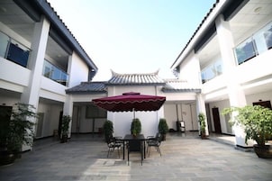 A courtyard with a table and chairs under a red umbrella, surrounded by potted plants.