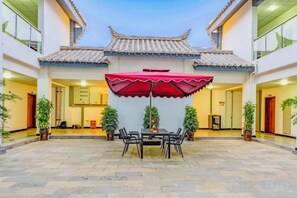 A courtyard with a traditional tiled roof, a table with chairs, and an umbrella. - Taowowo Holiday Hotel (Jianshui)