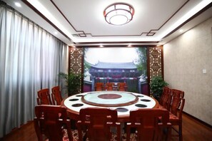 A conference room with a round table, chairs, and a view of a traditional building through a window. - Taowowo Holiday Hotel (Jianshui)