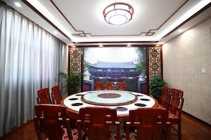 Un salón de conferencias con una mesa redonda, sillas y vista a un edificio tradicional a través de una ventana.