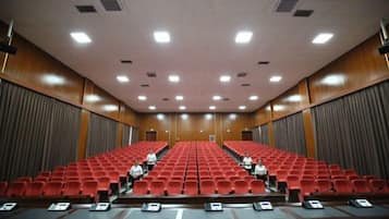 Un salón de conferencias con filas de sillas rojas, un atril al frente y una pantalla grande.
