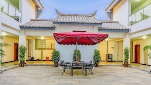 Um pátio com telhado tradicional em azulejos, uma mesa de jantar com cadeiras e um guarda-sol vermelho.