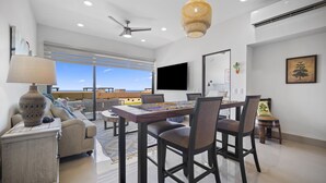Una sala de estar moderna con comedor, ventanas amplias, ventilador de techo y televisor montado.