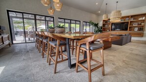 Un comedor amplio con una larga mesa de madera y sillas a juego, un televisor y una estantería en un interior moderno.