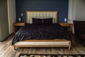 A bed with a tufted headboard, two bedside tables, and a patterned rug on a wooden floor. - Villa Esmeralda (Copacabana)