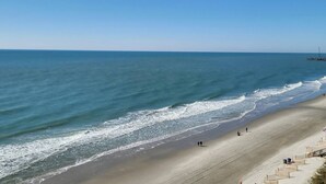 Ein Strand mit blauem Himmel, ruhiger See und einigen Menschen, die am Ufer entlanggehen.