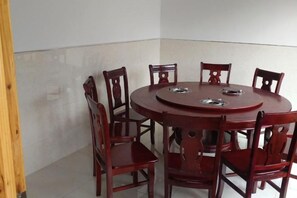 A round wooden dining table with six chairs, a white tiled floor, and a plain wall. - Grand Canyon View Inn (Enshi City)