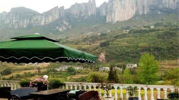 A terrace with a table and chairs, a green umbrella, and a view of mountains.