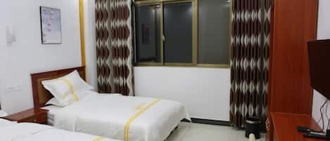 Habitación de hotel con dos camas, un escritorio, una silla, un televisor y una ventana con cortinas.