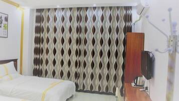 A hotel room with two beds, a wooden side table, a TV, and a wall-mounted air conditioning unit.