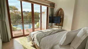 Un dormitorio con una cama grande, televisión y puerta corrediza de vidrio que da a una zona de piscina.