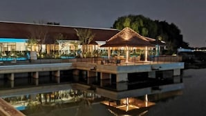 Un hotel frente al agua con bungalows sobre el agua, piscina y zona de restaurante.