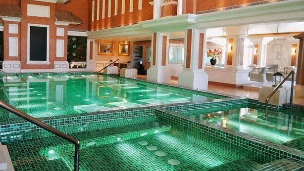Una amplia piscina interior con agua cristalina, rodeada por un muro de ladrillo y columnas blancas.
