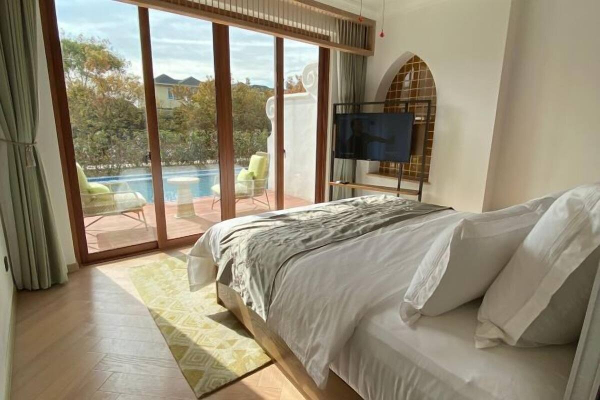 A bedroom with a bed, a TV, and a view of a swimming pool.