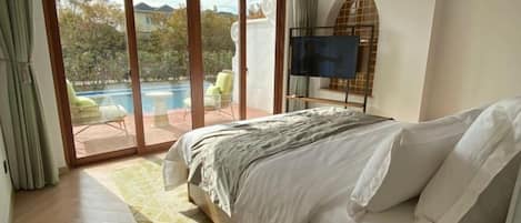 Un dormitorio con cama, televisión y vistas a una piscina.