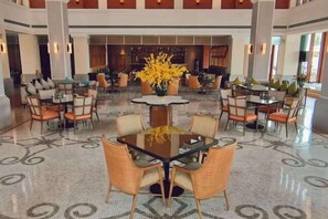 Vestíbulo de hotel con varias zonas de estar, que incluyen mesas redondas y sillas, y un jarrón decorativo en el centro.