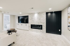 Un salon moderne avec un mur en marbre, un téléviseur à écran plat, une cheminée et un coin repas comprenant une table et des chaises.